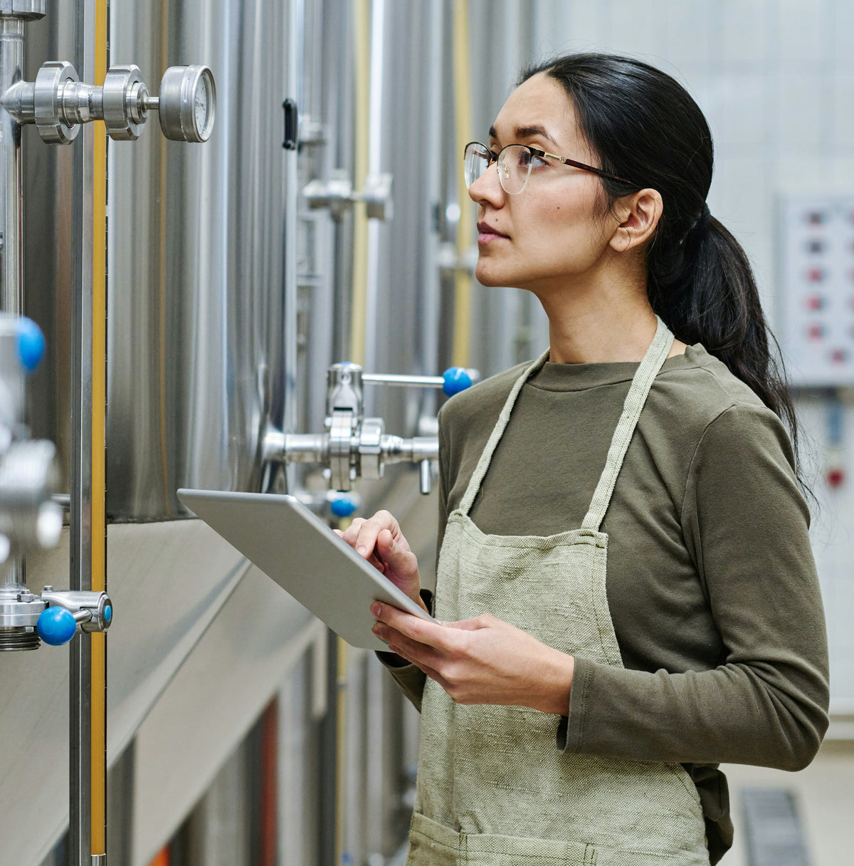 Person in a brewery wearing an apron and using a tablet computer.